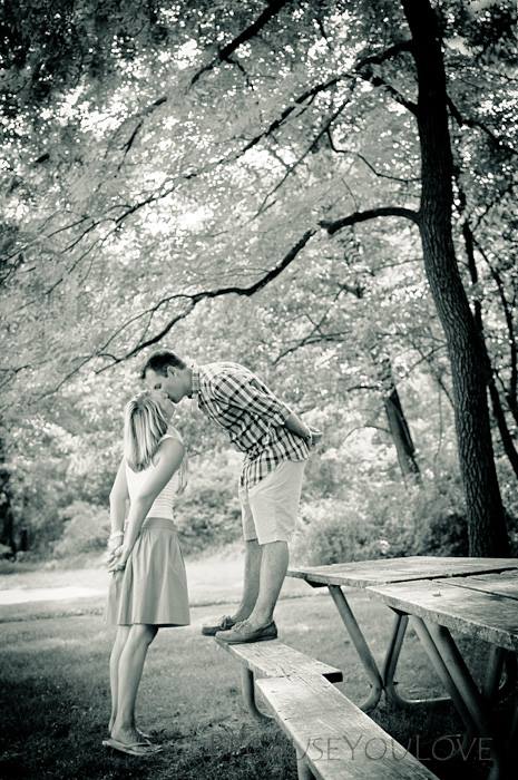 Groom stands on a park bench, kissing his bride-to-be.